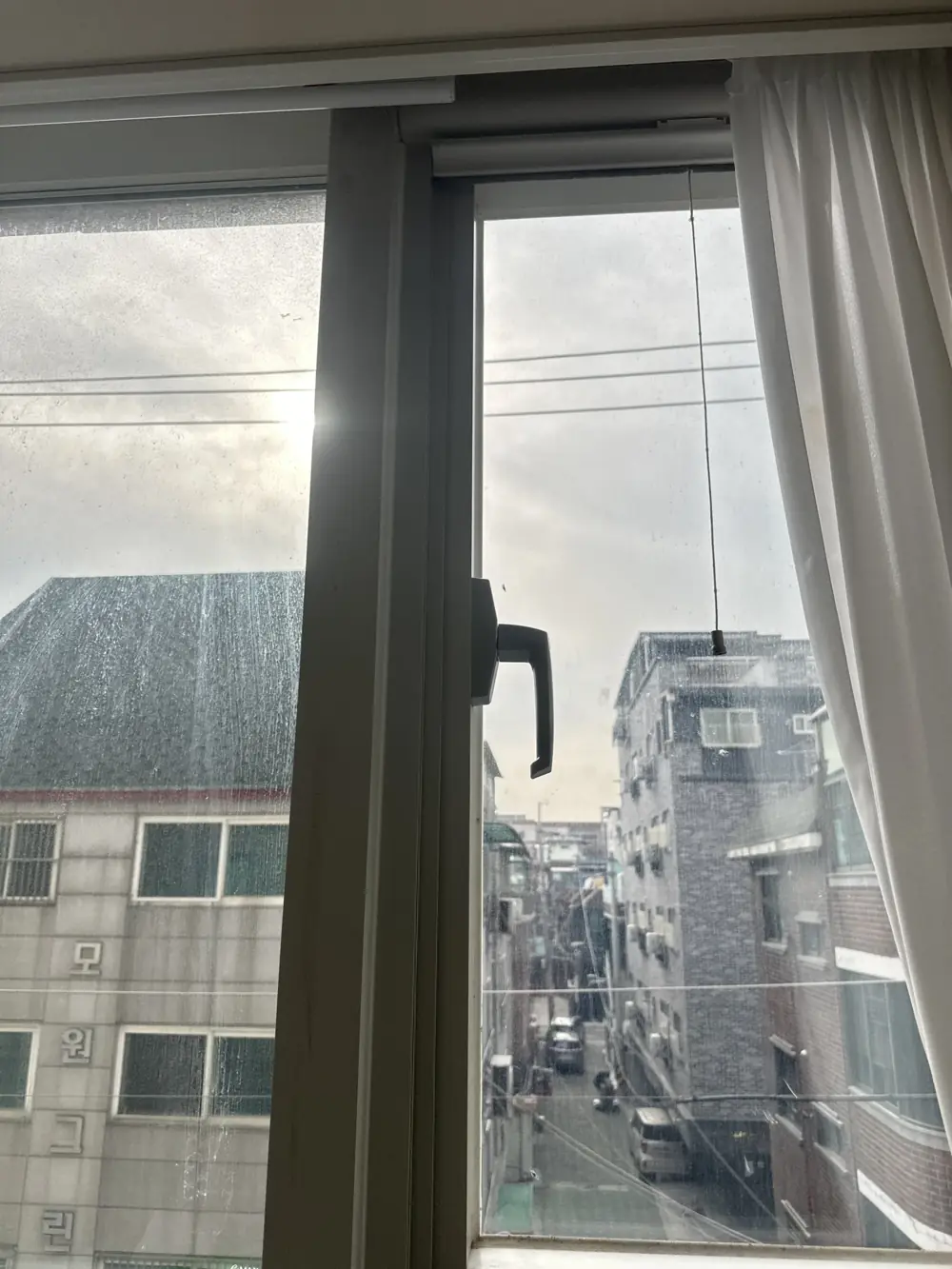 짙은 회색 레버형 손잡이를 새로 설치한 창문 이후 모습, 골목 풍경