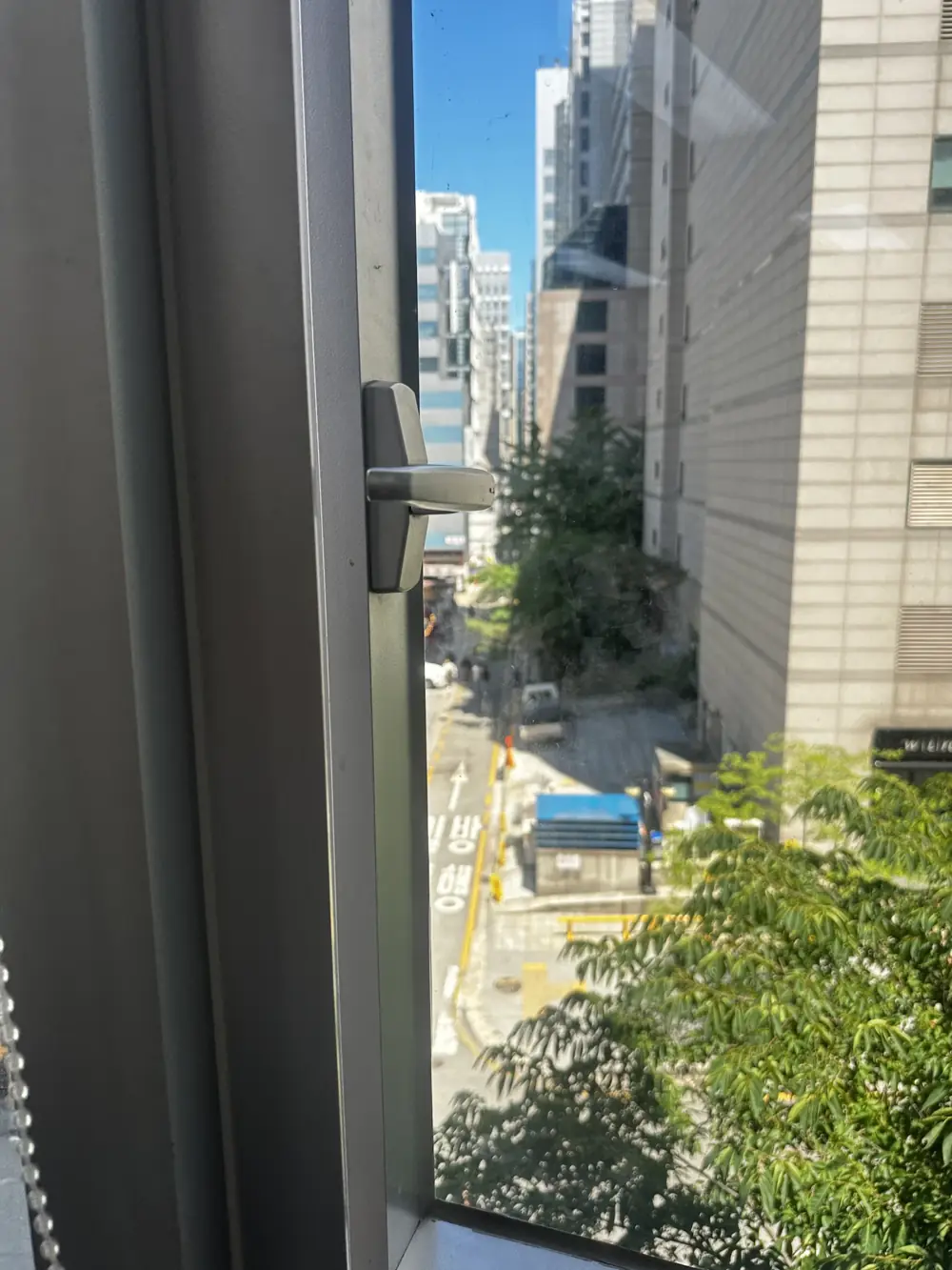 부러져 창이 열리지 않던 기존 T자형 창문 손잡이 교체 이전 모습, 도심 건물과 가로수
